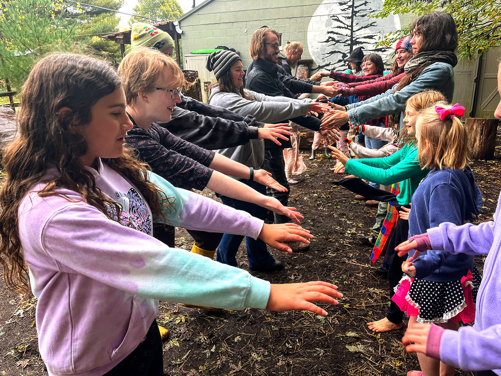 Two lines of dancers of all ages, with hands reaching out between the rows.