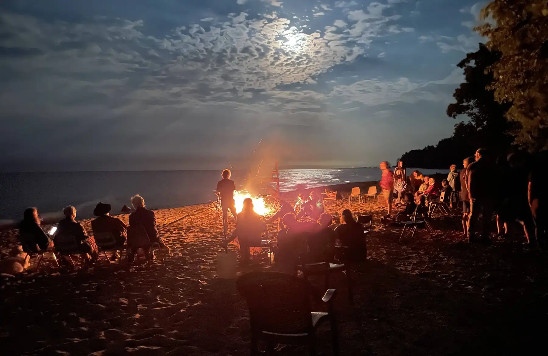 Campers around a campfire by a moonlit lake