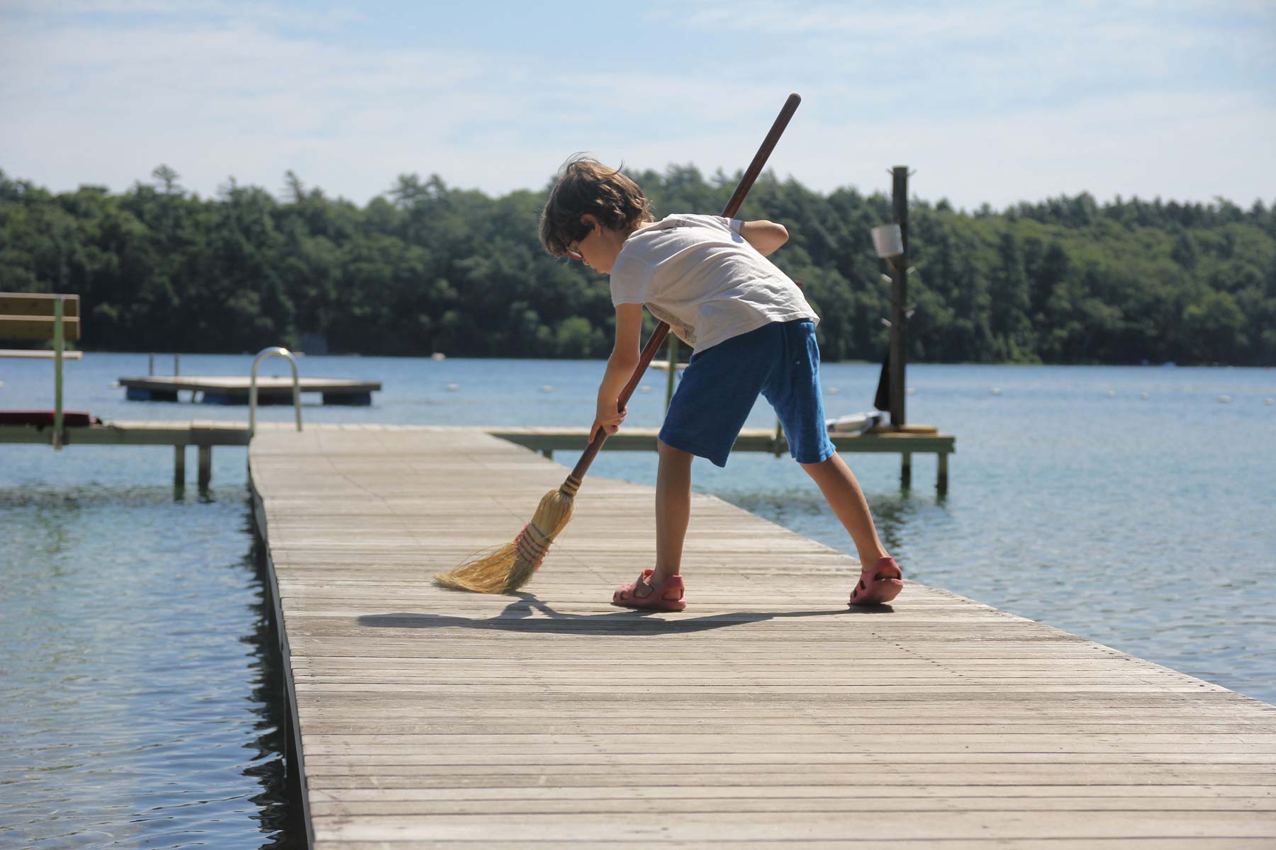 A young camper sweeps the dock over a lake