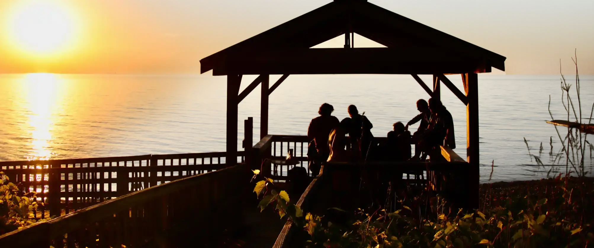 Musicians silhouetted against a sunset by the lakeside