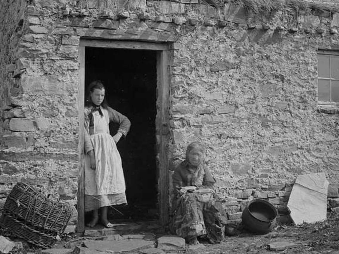 Women wait outside an Irish sod cottage