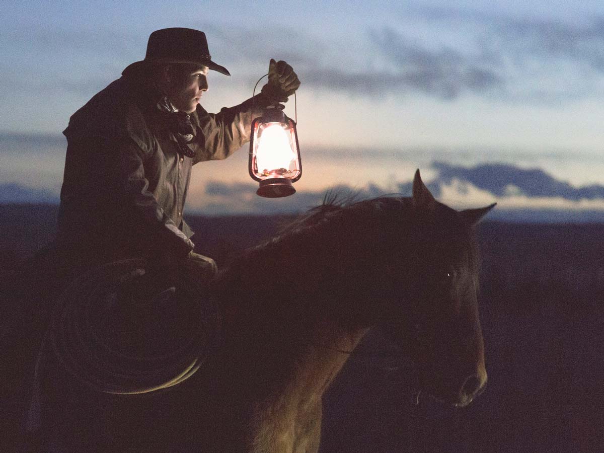 A cowboy on horseback keeps watch with a lantern
